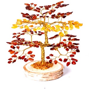 Può includere: Una scultura di albero in filo dorato con foglie di ambra in tonalità di rosso, arancio e giallo. L'albero è su una base di legno.