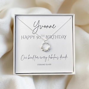 May include: Sterling silver necklace with a pendant featuring a ring with five small beads. The necklace is presented in a white box with the text "Yvonne HAPPY 50TH BIRTHDAY One bead for every fabulous decade".