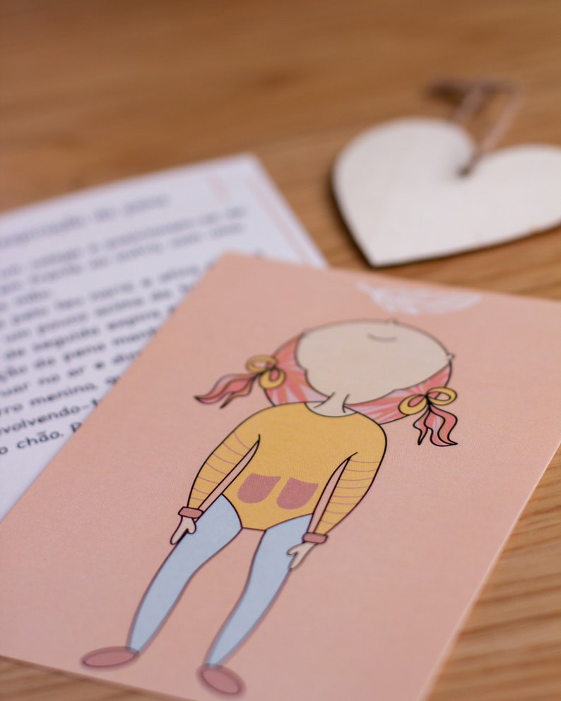 May include: A pink card with a cartoon illustration of a girl with pink hair wearing a yellow shirt with a pink pocket and blue pants. The girl is smiling and has her eyes closed.