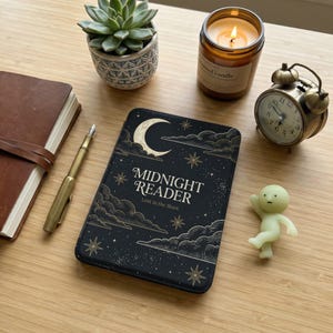 以下が含まれることがあります： 「MIDNIGHT READER」と「Lost in the Stars」の文字が白で書かれた黒い本の表紙。三日月と星のデザイン。他に、キャンドル、小さな時計、多肉植物、ペン、小さなフィギュアがあります。
