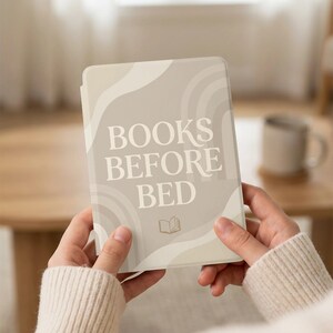 Op de afbeelding: Een lichtbeige e-reader hoes met de tekst "BOOKS BEFORE BED" in een schreeflettertype. De hoes heeft een golvend ontwerp in een lichtere beige kleur. Onderaan staat een klein boekicoon. De e-reader wordt met twee handen vastgehouden.
