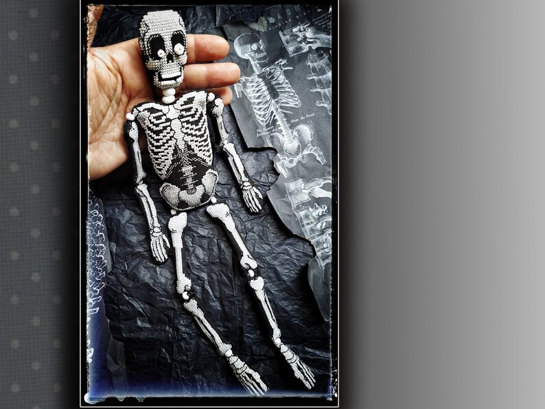 May include: A beaded skeleton doll with white beads and black thread. The doll is posed sitting with its legs crossed. The doll is on a black background.