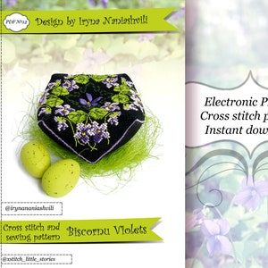 Op de afbeelding: Een zwart, vierkant kruissteekontwerp met paarse viooltjes en groene bladeren. Het ontwerp is omgeven door groene vezels en twee gele eieren. De tekst luidt "Biscornu Violets" en "Elektronisch PDF-bestand Kruissteekpatroon Direct downloaden."