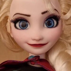 以下が含まれることがあります： 金髪、青い目、赤い唇のキャラクターの人形。人形は、緑色の宝石が付いた金の王冠と、金のトリムが付いた青と黒のドレスを着ています。人形は、子供向けのアニメ映画の人気キャラクターです。