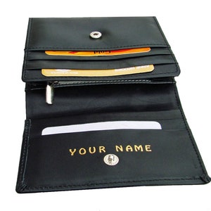 May include: Black leather wallet with a zippered compartment and multiple card slots. The wallet has a snap closure and a gold-colored inscription that reads "YOUR NAME".