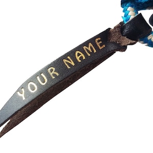 May include: A black leather strap with a gold inscription that reads "YOUR NAME".