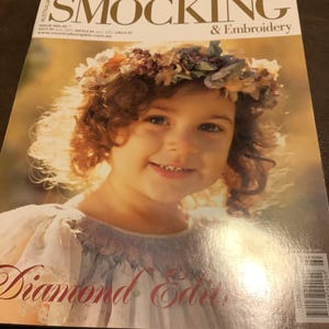 May include: A magazine cover featuring a smiling child wearing a floral crown. The magazine title reads "SMOCKING & Embroidery" with the text "Diamond Edition" below. The cover has a warm, golden color scheme.