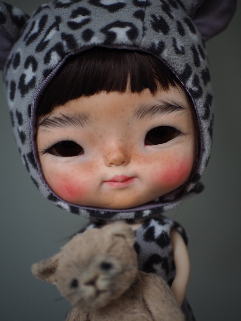 a doll holding a teddy bear wearing a leopard outfit