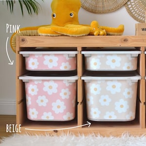 May include: Wooden storage unit with four bins, two in pink and two in beige, each adorned with a white daisy pattern. A large yellow octopus plush toy sits atop the unit, adding a playful touch to the storage solution.