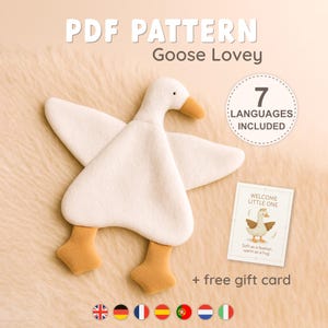 May include: A PDF pattern for a Goose Lovey, featuring a white plush goose with an orange beak and feet. The design includes 7 languages, a free gift card with the text Welcome Little One, Soft as a feather, warm as a hug, and flag icons.