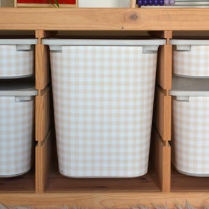 Pu&ograve; includere: Un contenitore rettangolare con un motivo a quadretti vichy beige chiaro e bianco, posizionato all'interno di uno scaffale in legno. Il contenitore presenta un bordo liscio di colore chiaro ed &egrave; affiancato da contenitori simili.