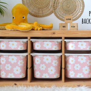May include: A wooden storage unit with six pink bins decorated with white daisy patterns. A large yellow octopus plush toy and a smaller one sit on top. The word blocks spell out "LOVE WE FUN".