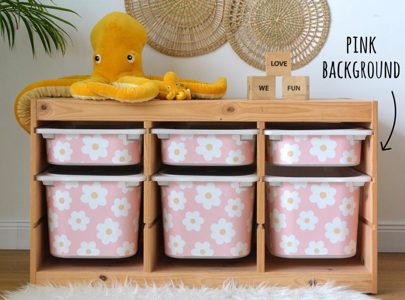 May include: A wooden storage unit with six pink bins decorated with white daisy patterns. A large yellow octopus plush toy and a smaller one sit on top. The word blocks spell out "LOVE WE FUN".