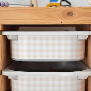 Pu&ograve; includere: Un mobile contenitore in legno chiaro con diversi contenitori rettangolari in plastica. Ogni contenitore &egrave; decorato con un motivo a quadretti vichy beige e bianco. L'unit&agrave; ha una struttura in legno naturale con ripiani aperti per i contenitori.