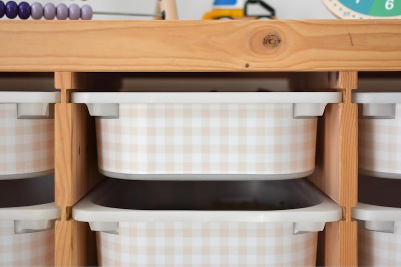 Pu&ograve; includere: Un mobile contenitore in legno chiaro con diversi contenitori rettangolari in plastica. Ogni contenitore &egrave; decorato con un motivo a quadretti vichy beige e bianco. L'unit&agrave; ha una struttura in legno naturale con ripiani aperti per i contenitori.