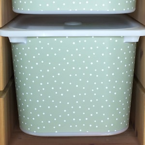 May include: A set of two green storage bins with white polka dots. The bins are made of plastic and have a white lid. The bins are sitting on a wooden shelf.