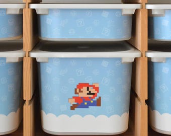 Puede incluir: Un conjunto de cubos de almacenamiento de plástico azul con tapas blancas. Los cubos tienen un patrón de personajes y símbolos de videojuegos. Los cubos están apilados uno encima del otro en una estantería de madera.