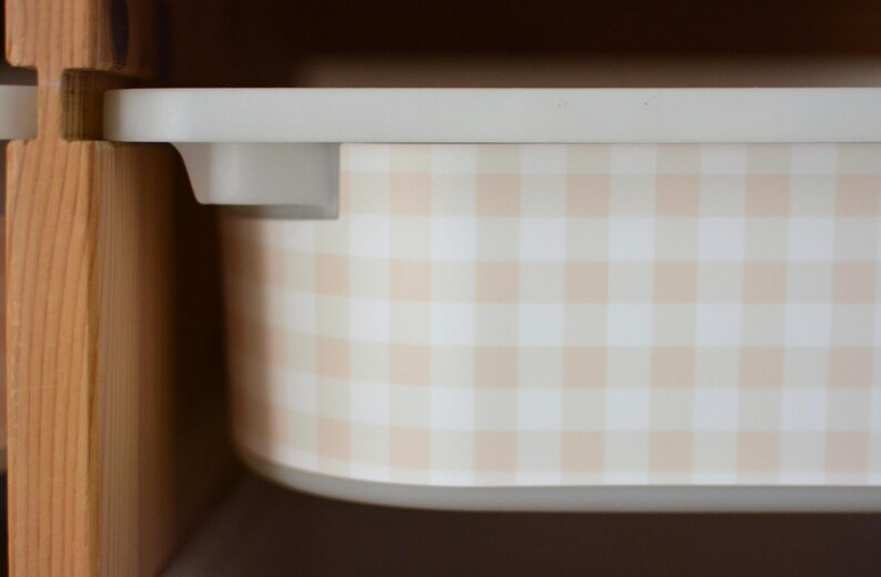 Pu&ograve; includere: Un contenitore rettangolare in plastica con un motivo a quadretti vichy color beige chiaro e bianco. Il contenitore presenta un bordo superiore liscio e piatto con angoli arrotondati, posizionato all'interno di una struttura in legno.