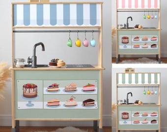 Può includere: Cucina giocattolo in legno con piano di lavoro verde chiaro e tenda a strisce blu e bianche. La cucina è dotata di lavello, tazze appese e torte e pasticcini giocattolo. Le parole "ENJOY LIFE" sono in alto.