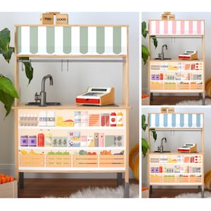 May include: Wooden play market stall with a striped awning, a sink, and a cash register. The shelves are stocked with toy groceries, including eggs, cheese, and produce. The awning is green and white. The words "FEEL GOOD" are on top.