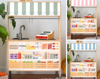 Può includere: Bancarella di mercato giocattolo in legno con tenda a strisce, lavandino e registratore di cassa. La bancarella presenta scaffali riforniti di generi alimentari giocattolo, tra cui frutta, verdura e prodotti confezionati. La tenda è verde e bianca. Le parole "FEEL GOOD" sono in alto.