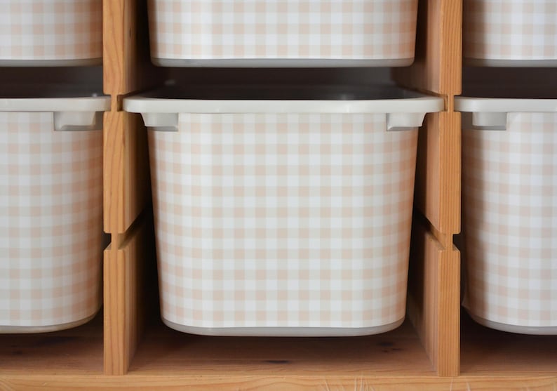 Pu&ograve; includere: Una serie di contenitori rettangolari con un motivo a quadretti vichy beige chiaro e bianco, organizzati all'interno di uno scaffale in legno chiaro. Ogni contenitore presenta un bordo liscio e arrotondato ed &egrave; posizionato in verticale.