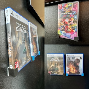 Op de afbeelding: Een verzameling videospel-hoezen, waaronder Dead Space, Final Fantasy XVI en Mario Kart 8 Deluxe. De hoezen worden getoond op een zwarte muur met magnetische houders.