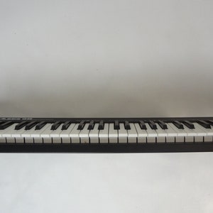 K&ouml;nnte beinhalten: Eine schwarze Tastatur mit wei&szlig;en Tasten ist auf einem Holzregal montiert. Das Regal ist an einer wei&szlig;en Wand befestigt.