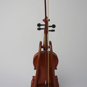 May include: A brown violin with a bow, resting on a wooden stand. The violin has a glossy finish and black tuning pegs. The bow is held in place by the stand. The stand is made of wood and has a simple, elegant design.