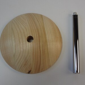 May include: A wooden base with a hole in the center and a chrome metal rod. The base is light brown and has a wood grain pattern. The rod is smooth and shiny.