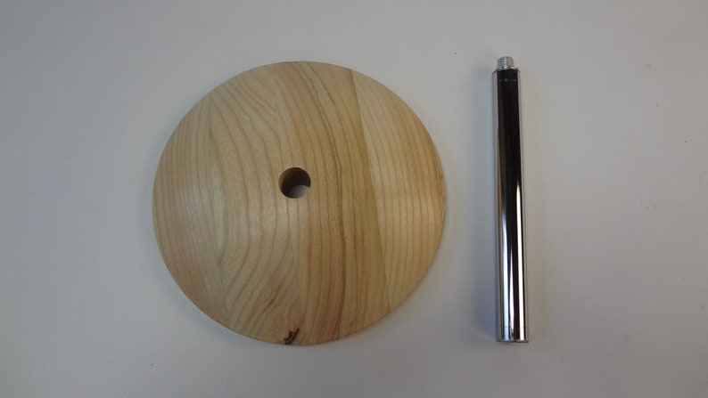 May include: A wooden base with a hole in the center and a chrome metal rod. The base is light brown and has a wood grain pattern. The rod is smooth and shiny.