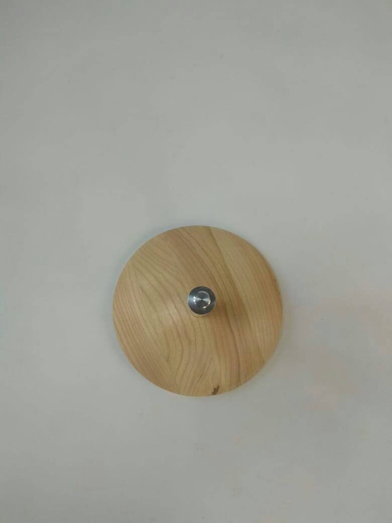 May include: A round wooden lid with a silver knob in the center. The lid is light brown with a wood grain pattern.