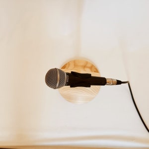 May include: A silver microphone with a black cable attached to a wooden stand. The microphone is on a white surface.