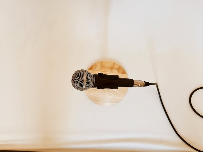 May include: A silver microphone with a black cable attached to a wooden stand. The microphone is on a white surface.