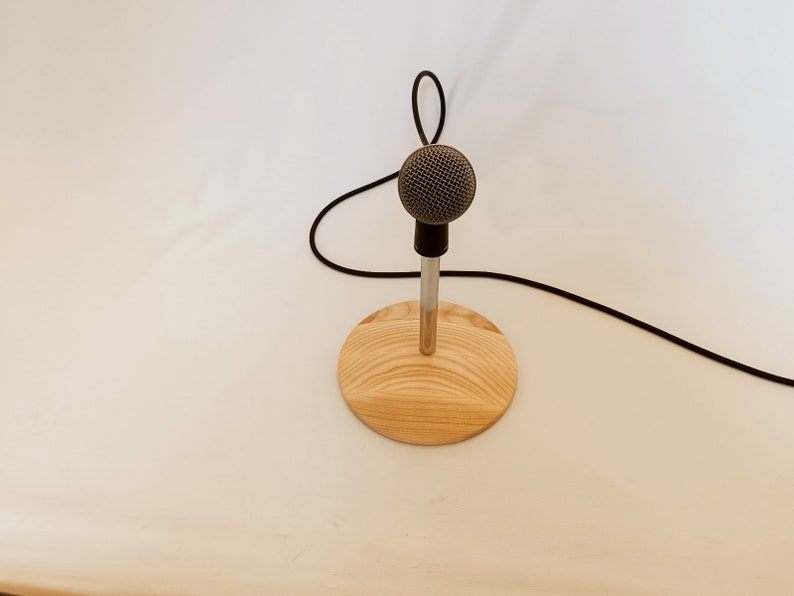 May include: A silver microphone on a wooden stand with a black cable.