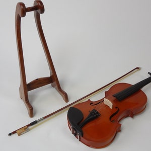 May include: A wooden violin with a bow and a wooden stand. The violin is a warm brown color with black details. The bow is light brown. The stand is a dark brown, arched shape.