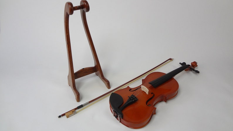 May include: A wooden violin with a bow and a wooden stand. The violin is a warm brown color with black details. The bow is light brown. The stand is a dark brown, arched shape.