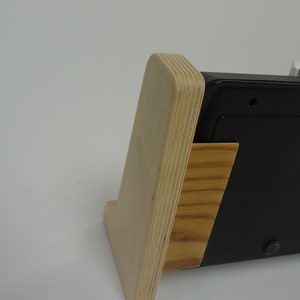 K&ouml;nnte beinhalten: Ein Holzst&auml;nder mit einem schwarzen elektronischen Ger&auml;t. Der St&auml;nder ist aus Sperrholz und hat eine nat&uuml;rliche Holzoptik. Das Ger&auml;t ist rechteckig und hat eine schwarze Oberfl&auml;che.