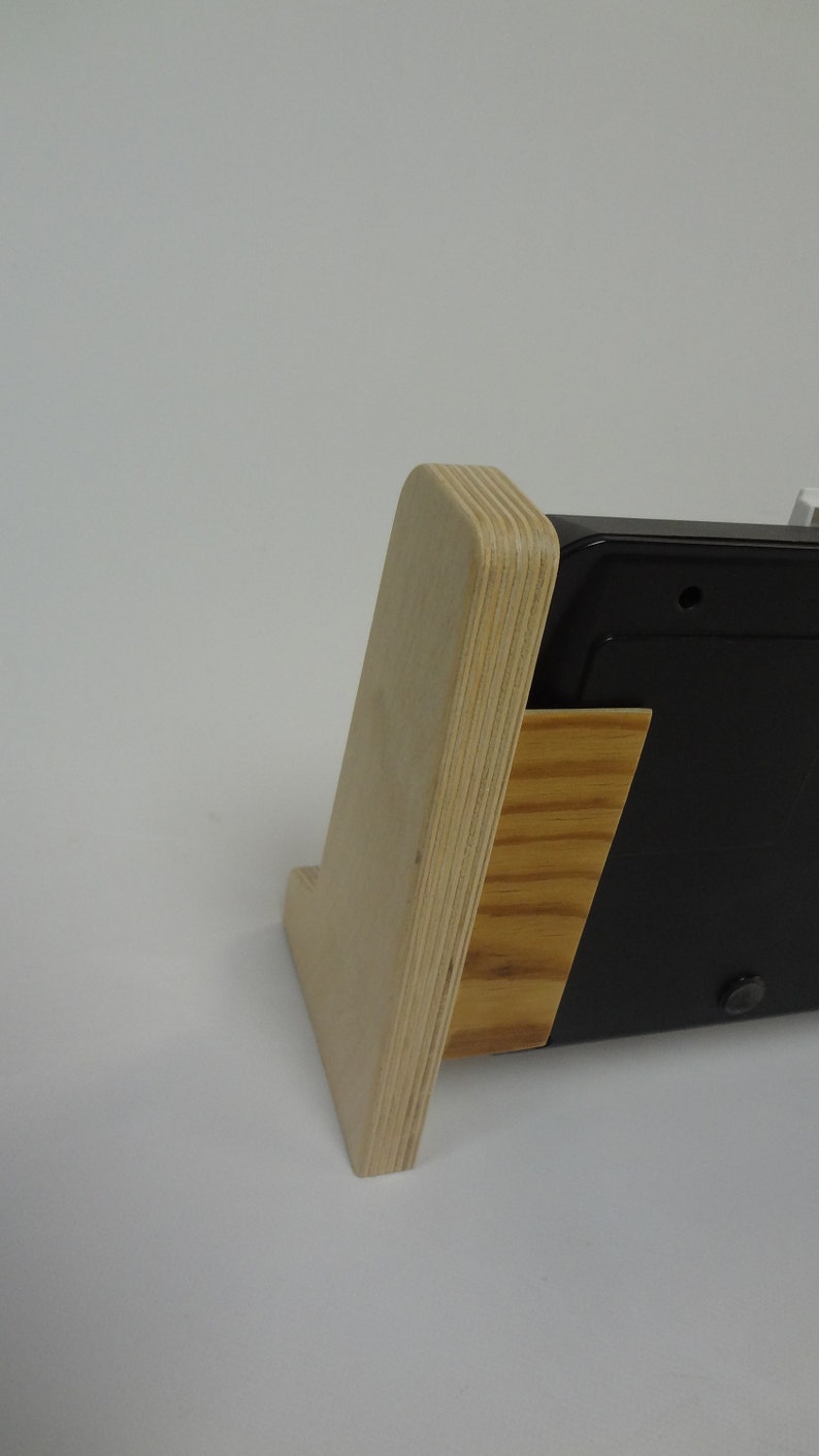 K&ouml;nnte beinhalten: Ein Holzst&auml;nder mit einem schwarzen elektronischen Ger&auml;t. Der St&auml;nder ist aus Sperrholz und hat eine nat&uuml;rliche Holzoptik. Das Ger&auml;t ist rechteckig und hat eine schwarze Oberfl&auml;che.