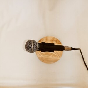 May include: A black microphone with a silver grill is mounted on a wooden stand. A black cable is connected to the microphone.