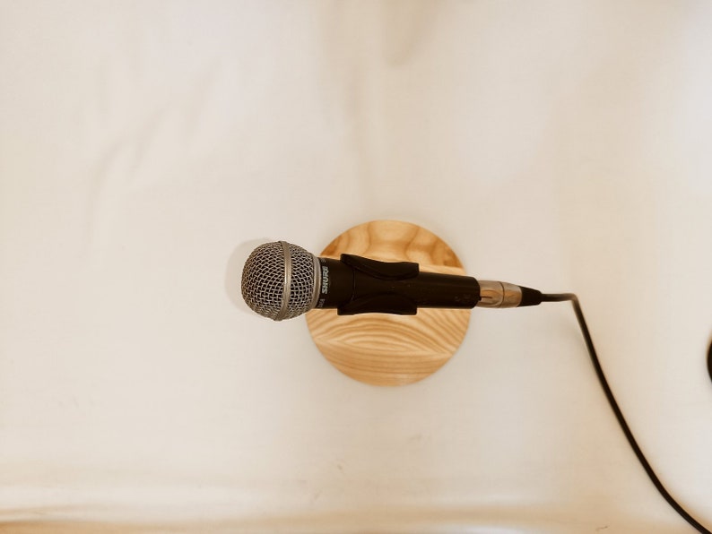 May include: A black microphone with a silver grill is mounted on a wooden stand. A black cable is connected to the microphone.