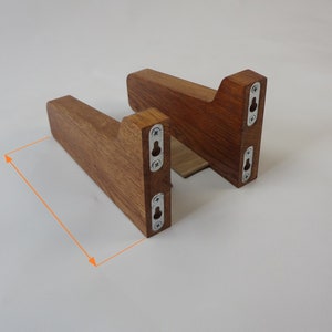 K&ouml;nnte beinhalten: Zwei Holz-Regalhalterungen mit einer dunkelbraunen Beize. Die Halterungen sind 10 cm breit und haben jeweils drei Schraubenl&ouml;cher. Die Halterungen sind aus massivem Holz gefertigt und haben einen rustikalen Look.