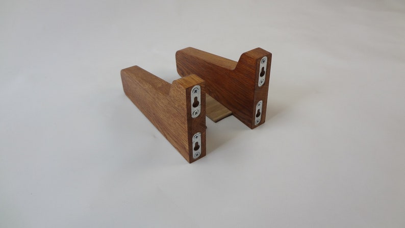 K&ouml;nnte beinhalten: Zwei Holz-Regalbretter mit einer dunkelbraunen Beize. Jedes Brett hat drei Metallschraubenl&ouml;cher auf der R&uuml;ckseite.