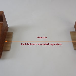 K&ouml;nnte beinhalten: Zwei Holz-Regalhalter mit hellbrauner Oberfl&auml;che. Jeder Halter ist separat montiert und kann verwendet werden, um ein Regal in jeder Gr&ouml;&szlig;e zu erstellen.  "Any size" und "Each holder is mounted separately" sind in roter Schrift unter den Haltern geschrieben.
