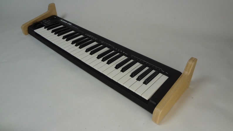 K&ouml;nnte beinhalten: Eine schwarze Tastatur mit wei&szlig;en Tasten und einem Holzst&auml;nder. Die Tastatur tr&auml;gt den Schriftzug "Alesis Q88".