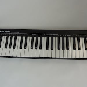 K&ouml;nnte beinhalten: Eine schwarze Alesis Q49-Tastatur mit 49 Tasten, zwei Drehkn&ouml;pfen und zwei Tasten. Die Tastatur ist auf zwei Holzst&auml;ndern montiert.