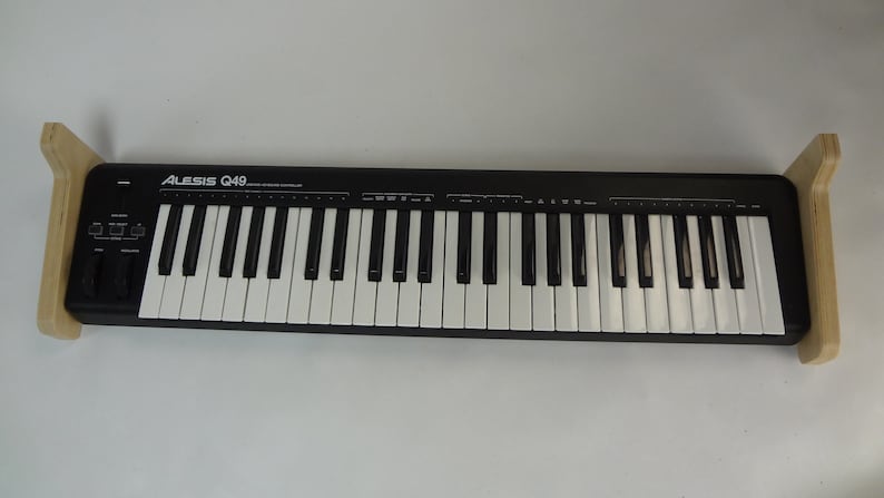 K&ouml;nnte beinhalten: Eine schwarze Alesis Q49-Tastatur mit 49 Tasten, zwei Drehkn&ouml;pfen und zwei Tasten. Die Tastatur ist auf zwei Holzst&auml;ndern montiert.