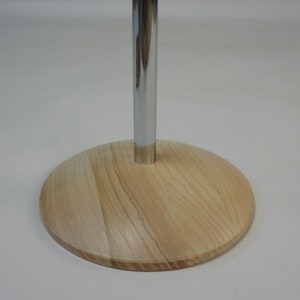 May include: A wooden base with a chrome metal rod extending upwards. The base is light brown with a wood grain pattern.