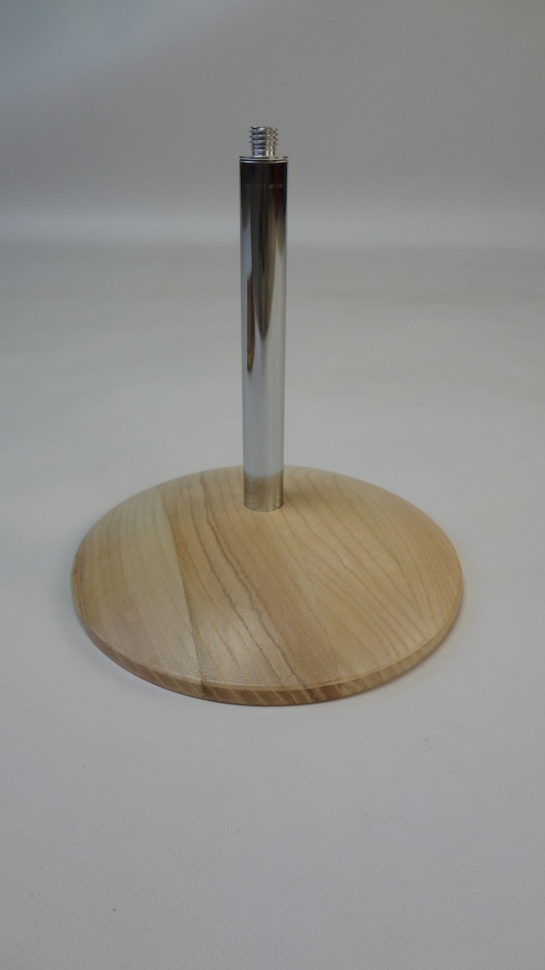 May include: A wooden base with a chrome metal rod extending upwards. The base is light brown with a wood grain pattern.