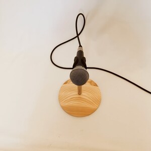 May include: A black microphone on a wooden stand with a black cable.